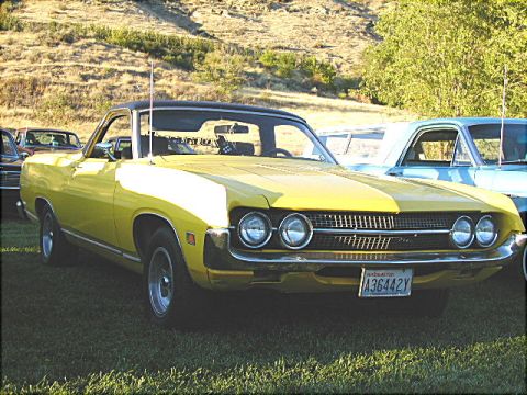 1967 Ford Ranchero - A yellow pickup truck with a black vinyl top is parked on a grassy field with a hill in the background.
