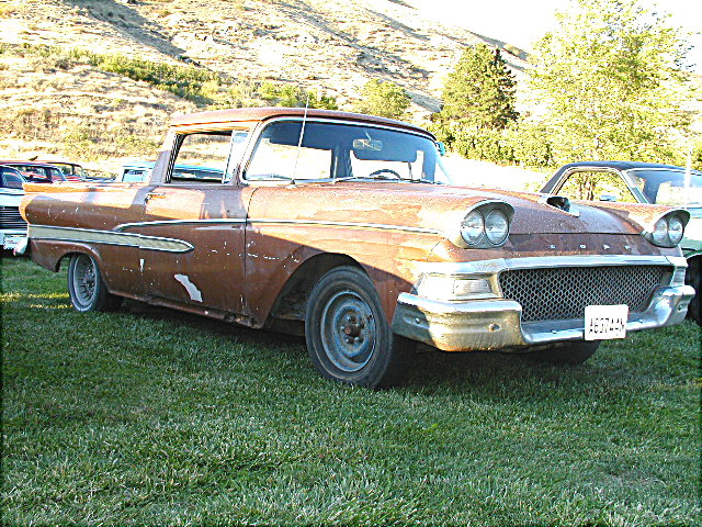 Rusty patina late-1950s Ford Ranchero pickup parked on grass at a car show