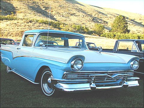 1967 Ford Ranchero - A classic two-tone blue and white 1957 Ford Ranchero pickup truck is parked on grass with a hillside in the background.
