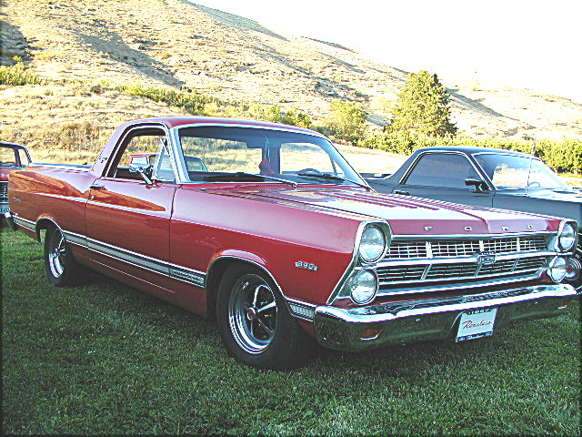 Red 1967 Ford Ranchero, front 3/4 view, parked on grass with hill behind.