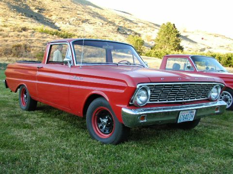 1967 Ford Ranchero - A red 1967 Ford Ranchero pickup truck is parked on grass with a second vehicle visible behind it.