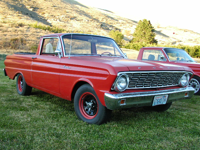 Red 1960s Ford Ranchero pickup on grass, chrome grille and black steel wheels