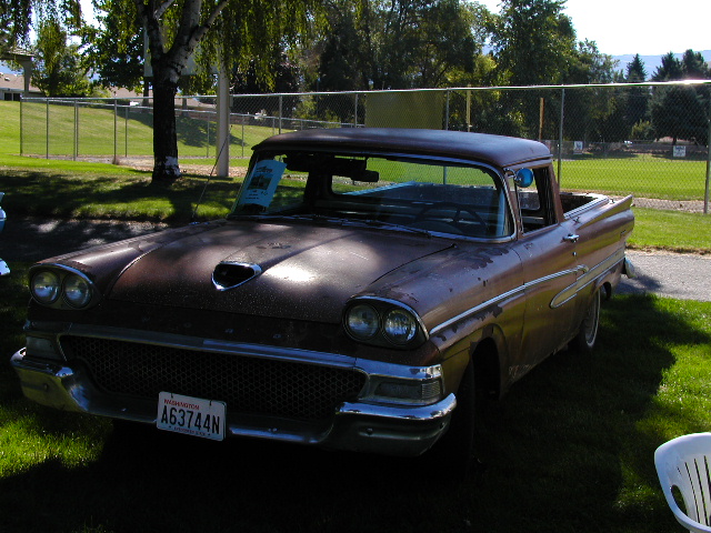 Patina-brown 1950s Ford Ranchero pickup with quad headlights parked on grass at a show