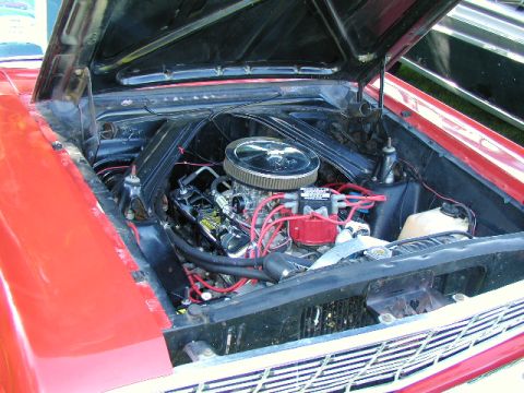 1967 Ford Ranchero - The engine bay of a red Ford Falcon, a V8 engine with a chrome air cleaner and red spark plug wires.
