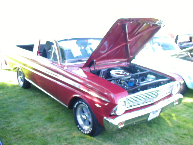 Red 1960s Ford Ranchero pickup on grass with hood open showing V8 engine