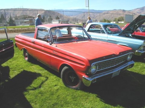 1967 Ford Ranchero - A red 1965 Ford Ranchero pickup truck is parked on grass at an outdoor event with other vehicles.