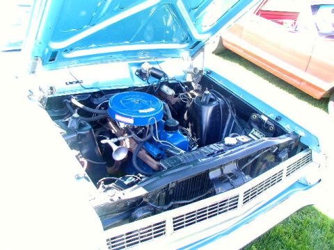 1967 Ford Ranchero - The engine bay of a 1967 Ford Ranchero, its blue air cleaner and engine components, with another vehicle visible in the background.
