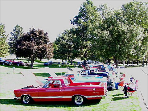 1967 Ford Ranchero - Several classic vehicles are lined up on a grassy field under trees, with people relaxing nearby.