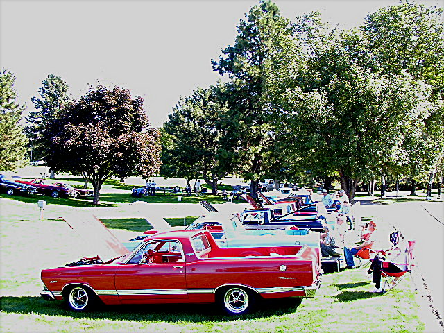 Red late-1960s Ford Ranchero parked in profile at a grassy park car show