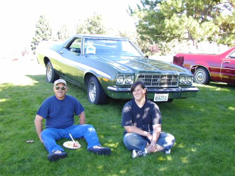 1967 Ford Ranchero - Two people relax on the lawn next to a green Ford Ranchero, with another vehicle visible in the background.