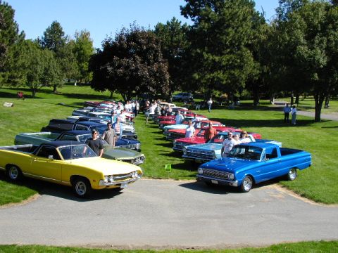 1967 Ford Ranchero - A gathering of classic pickup trucks and cars displayed on a sunny day in a park-like setting.