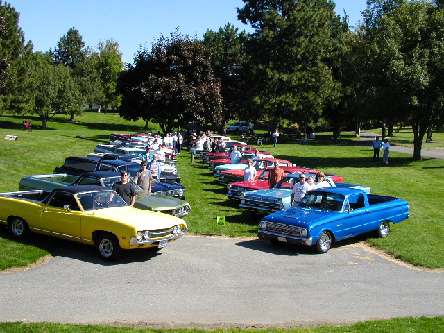 Yellow and blue pickup trucks parked in a line with other vehicles on a grassy field
