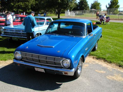 1967 Ford Ranchero - A bright blue Ford Ranchero pickup truck is parked on asphalt next to a light blue car at an outdoor event.