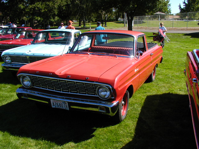 Red Ford Ranchero pickup parked on grass, with a light blue pickup and other cars behind it. License plate A76401R