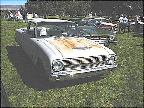 1967 Ford Ranchero - A classic white Ford Falcon Ranchero with a prominent grille and rusty hood is displayed on a grassy field alongside other vehicles.