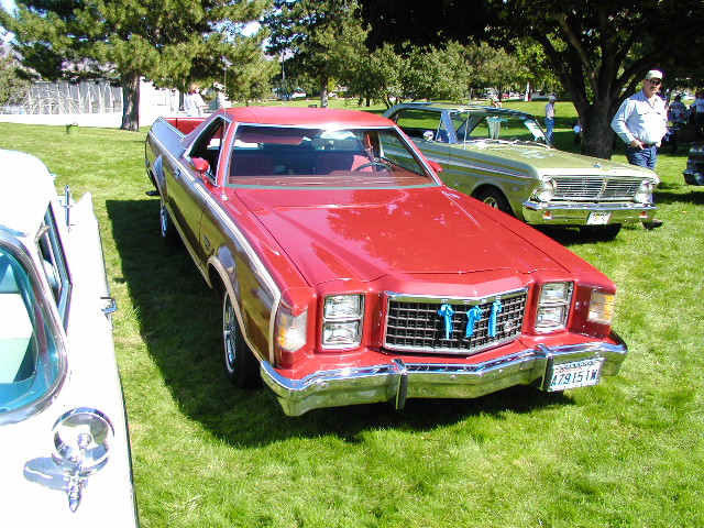 red pickup truck with blue ribbons on grille, parked on grass next to a green car