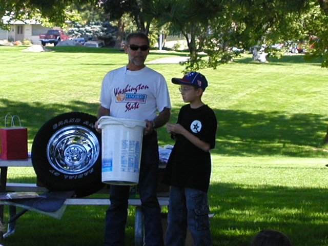 Raffle drawing at a park picnic table with a tire on a chrome wheel leaning nearby