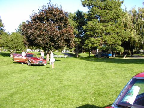 1967 Ford Ranchero - A red 1977 Ford Ranchero is parked on grass with people around it; a blue truck is in the background.