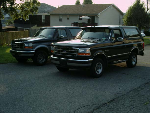 Two dark green two-door Ford Broncos parked on a driveway at a 3/4 front angle