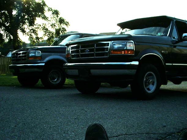 Low-angle dusk shot of two 90s Ford Broncos nose-out, chrome grilles and steel wheels