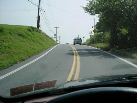 1992 Ford Bronco - A truck travels down a two-lane road bordered by grassy hills and trees under a hazy sky.