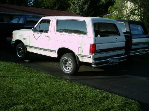 1988 Ford Bronco - A white Ford Bronco is parked on a driveway next to another vehicle.