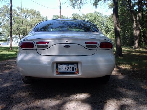 2000 Ford Taurus - Rear view of a white 2000 Ford Taurus parked on a dirt road with trees in the background.