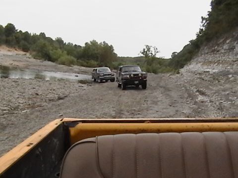 1986 Ford Bronco - Two SUVs navigate a rocky, off-road path under an overcast sky.