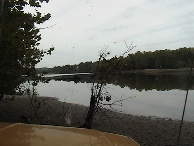 View of a river and trees from inside a vehicle, with a partial view of the dashboard and windshield
