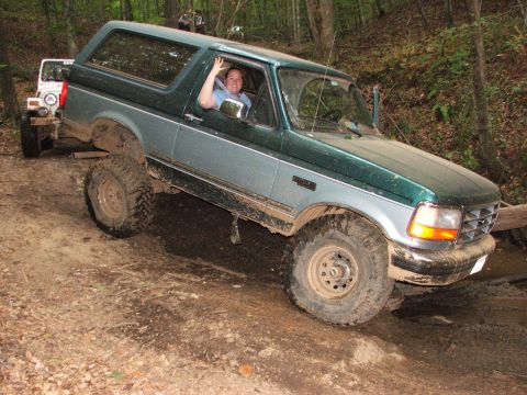 1996 Ford Bronco - A two-tone green and blue 1996 Ford Bronco tackles a challenging off-road course with a second vehicle visible behind it.