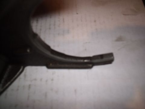 1985 Ford Bronco - Soft-focus close-up of one prong of a cast metal shift fork lying on a sheet of white paper, showing the worn wear pad along the inner curv…