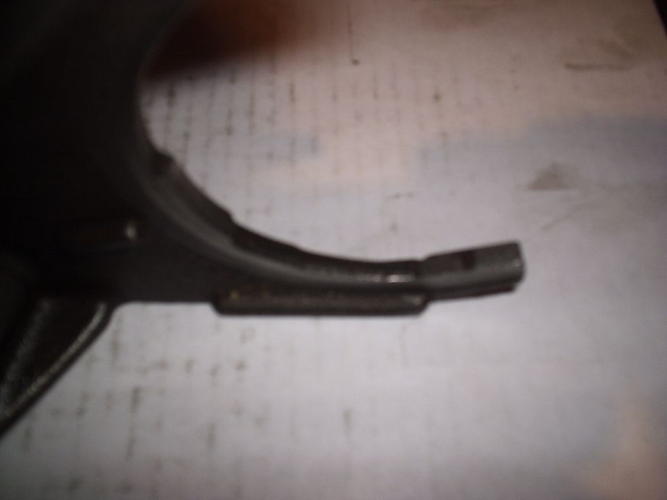 Close-up of a shift fork prong with a worn wear pad, lying on white paper