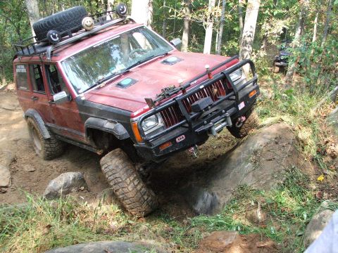 1996 Ford Bronco - A red Jeep Cherokee XJ navigates a rocky trail, with another vehicle visible in the background.