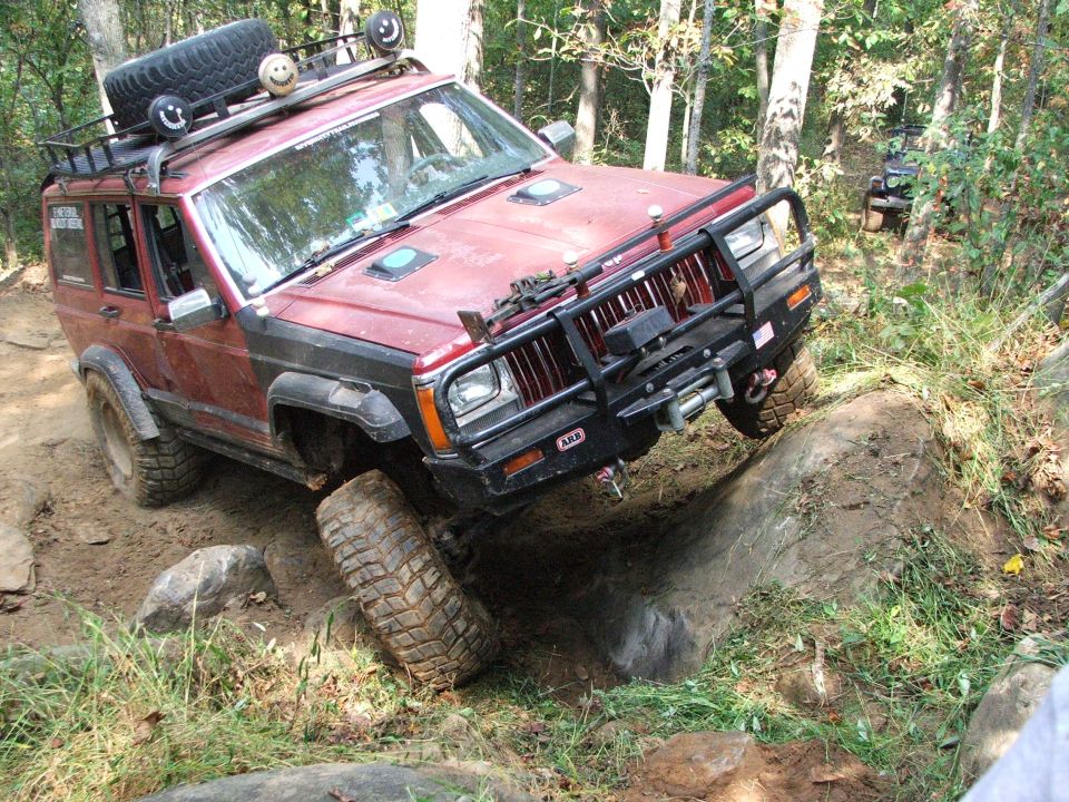 Red Jeep Cherokee XJ off-roading over rocks, front bumper with winch, roof rack with spare tire
