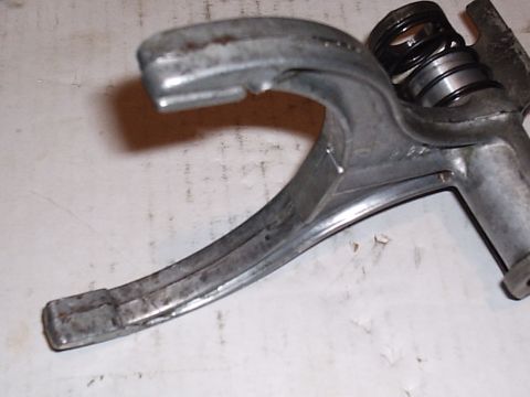 1985 Ford Bronco - A cast aluminum shift fork removed from a gearbox, showing the worn contact faces on both prongs and a detent spring with washers on the sh…