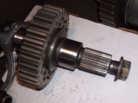 1985 Ford Bronco - Close-up of a transmission or transfer case shaft with a large helical drive gear pressed on, a polished bearing journal, external splines…