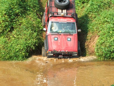 1996 Ford Bronco - Red Jeep Cherokee navigates a water crossing on an off-road trail.