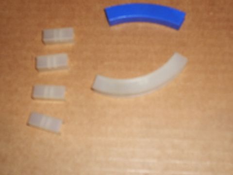 1985 Ford Bronco - Four small white nylon shift-fork pads and two curved plastic fork inserts, one blue, one white, laid out on a cardboard surface. The piece…