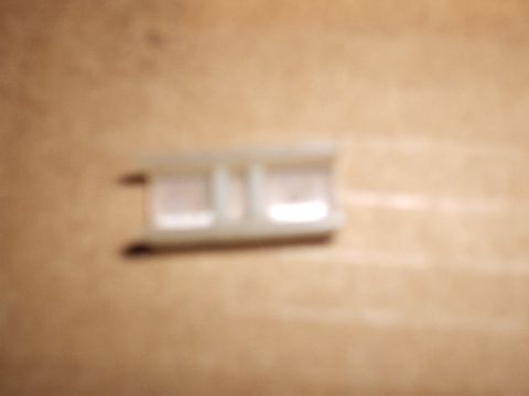 1985 Ford Bronco - Blurry close-up of a single small white nylon shift-fork wear pad sitting alone on a cardboard surface, with a molded center rib and clip c…