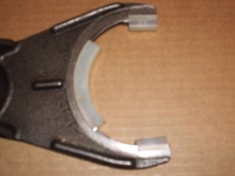 1985 Ford Bronco - Close-up of a cast transfer case shift fork fitted with fresh white nylon wear pads, a long curved insert on the inner arc plus two block p…
