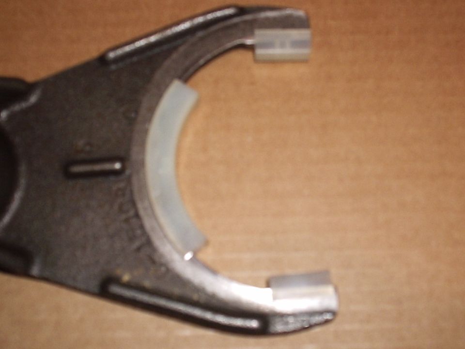 Cast shift fork with new white nylon wear pads installed, on cardboard