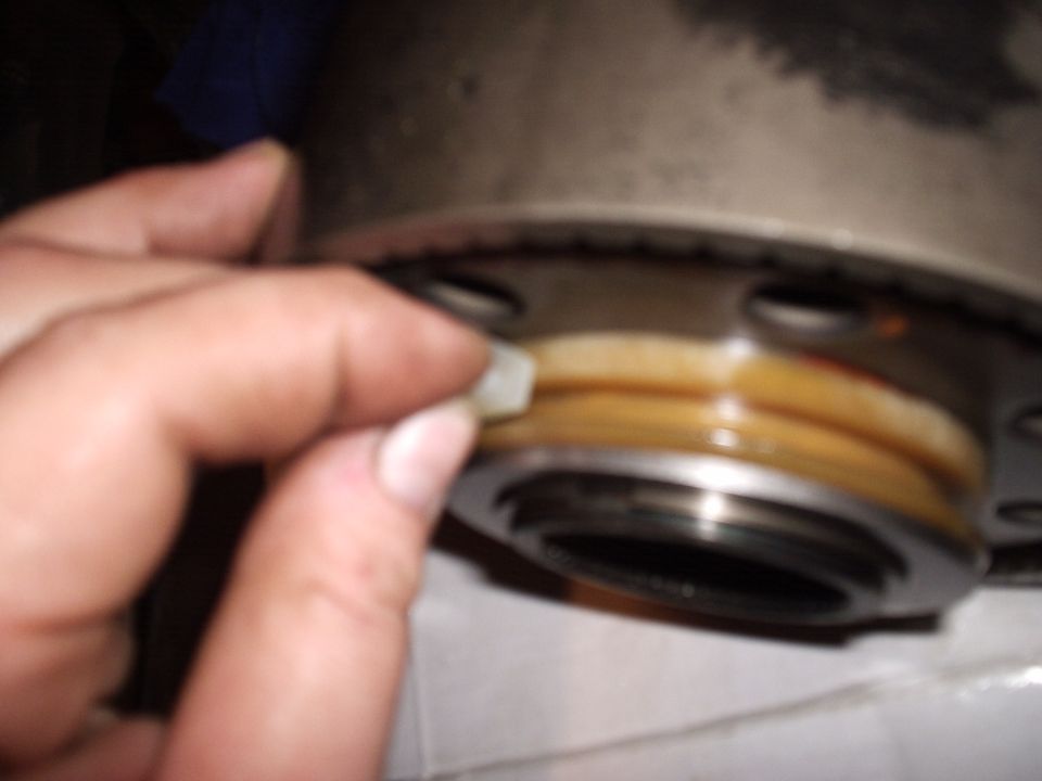 Hand holding a small white plastic wear pad beside a transmission gear with brass synchro rings