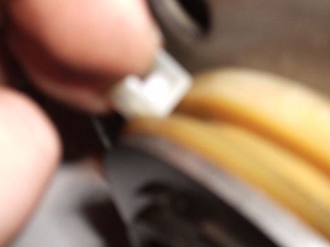 1985 Ford Bronco - Extreme, out-of-focus macro of fingers holding a small white nylon shift-linkage clip or bushing against a dark metal lever, with a yellow-…
