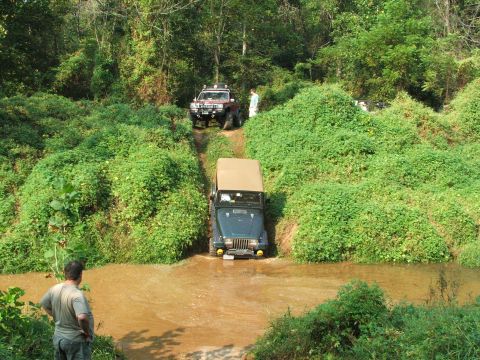 1996 Ford Bronco - Two off-road vehicles navigate a wooded trail with a water crossing.