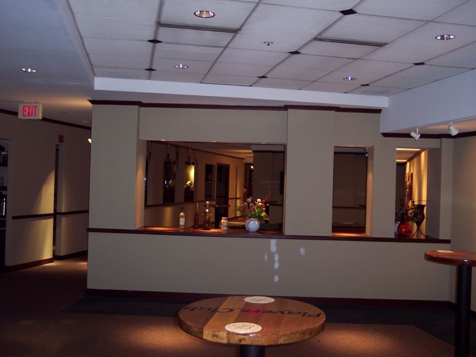 Interior of a building with an exit sign, a counter with bottles and flowers, and a round table