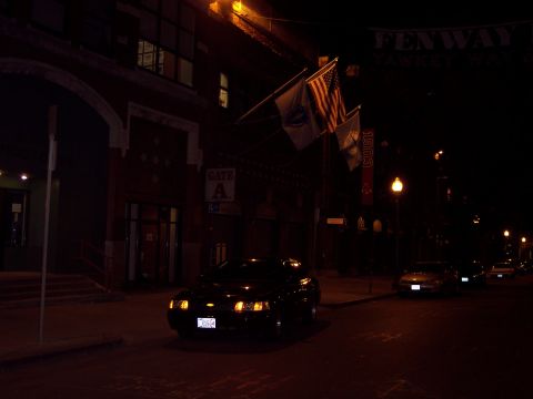 2001 Ford Crown Victoria - A dark sedan is parked on a street at night, with flags flying above a building entrance.
