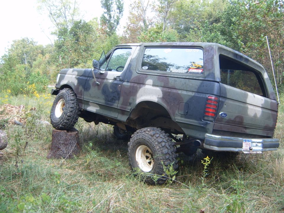 Camouflaged Ford Bronco with lifted suspension is driving over a tree stump off-road
