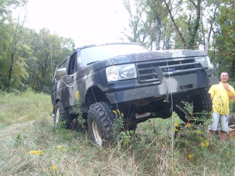 1988 Ford Bronco - A man poses with a lifted Ford Bronco, modified for off-road use, parked in a grassy, wooded area.