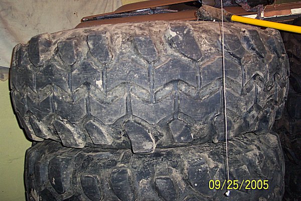 Stack of two large, off-road tires with aggressive tread patterns, covered in dirt