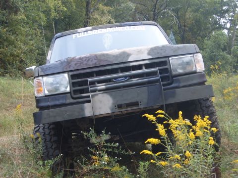 1988 Ford Bronco - A camouflaged Ford Bronco is parked off-road with yellow wildflowers in the foreground.
